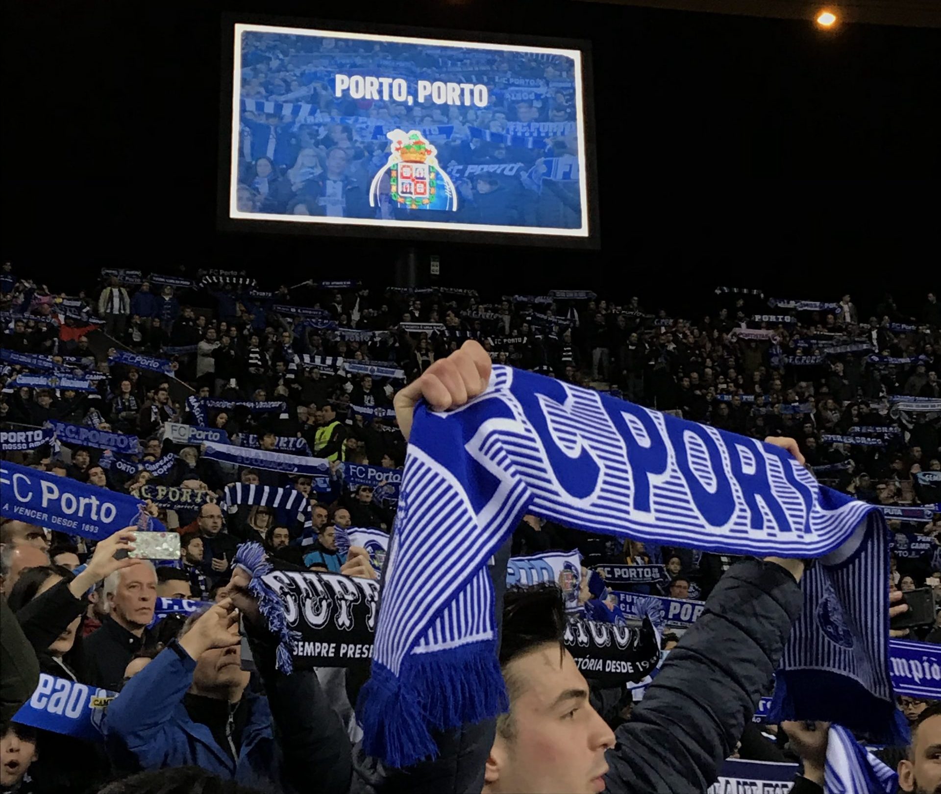 Man holds up a Porto team scarf while attending a soccer match at the Estadio Dragões.